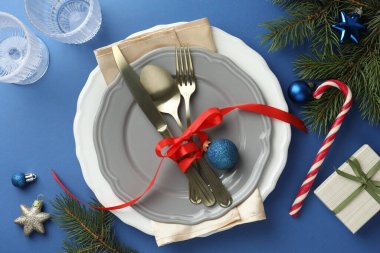 Tabakları, şık çatal bıçakları ve mavi masasında şenlikli dekorları olan güzel bir Noel ortamı.