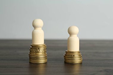Finansal eşitsizlik. Ahşap masada insan figürleri ve madeni paralar