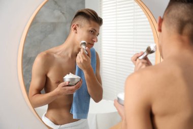 Banyoda aynanın yanında tıraş köpüğü kullanan yakışıklı bir adam.