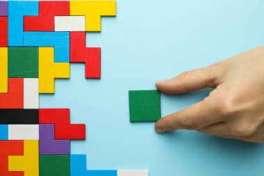 Açık mavi arka planda renkli ahşap yapboz parçalarıyla oynayan kadın, üst görünüm