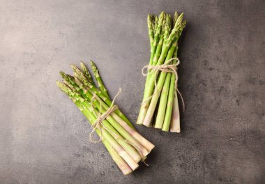 Taze yeşil kuşkonmaz demetleri gri desenli masa üzerinde düz uzanır.