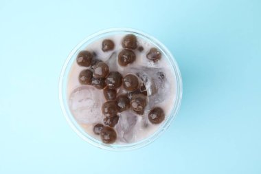 Açık mavi arka planda plastik bardakta lezzetli sütlü çay, üst manzara.