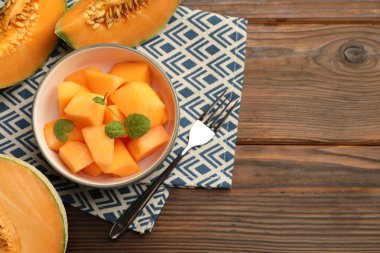 Olgun kavun parçaları kasede ve çatalla ahşap masada, düz yerde. Metin için boşluk