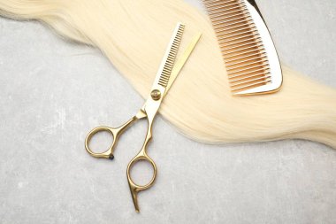 Sarı saç teli, tarak ve profesyonel makas gri masada, üst tarafta.