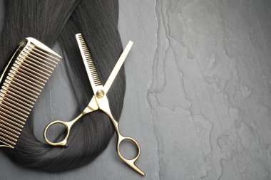 Gri yüzeyde siyah saç teli, tarak ve profesyonel makas düz yerde. Metin için boşluk