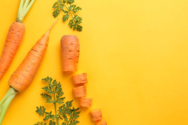 Sarı arka planda yeşil yapraklı taze havuçlar, düzlük. Metin için boşluk