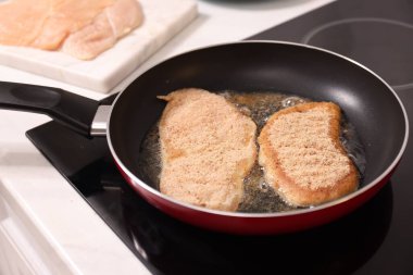 Cooking schnitzel in frying pan on stove, closeup clipart