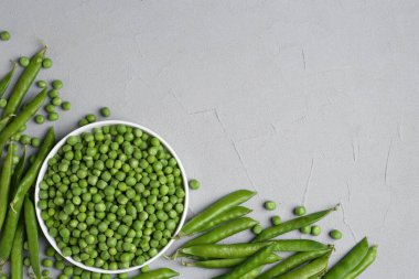 Taze yeşil bezelyeler ve kabuklar gri masada, düz yerde. Metin için boşluk