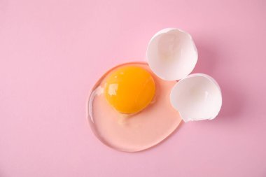 Kırık çiğ yumurta, pembe arka planda kabuk, üst manzara.