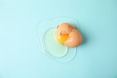 Broken raw egg with shell on light blue background, top view clipart