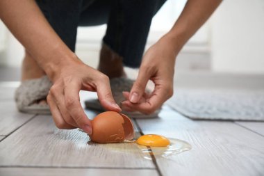 Kapalı alandaki gri ahşap zeminden kabuk ve kırık yumurta çıkaran kadın.