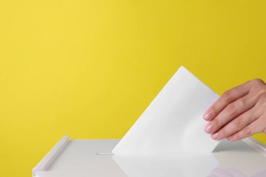 Kadın oyunu sarı arka plana karşı sandığa koyuyor, yakın plan. Metin için boşluk