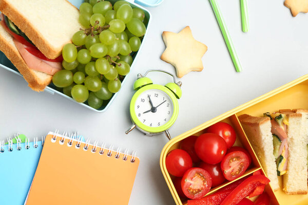 Lunch box with snacks, alarm clock and stationery on white background, flat lay