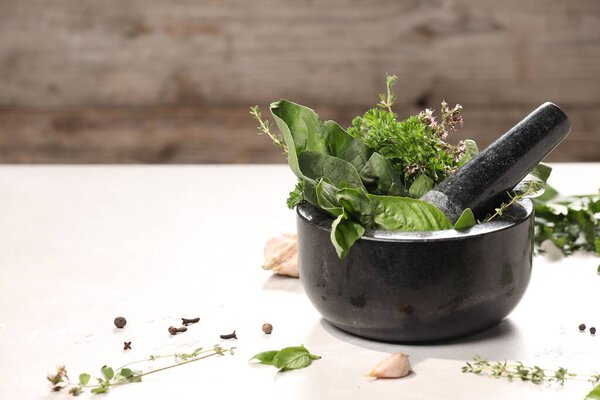 Mortar with different aromatic herbs on white table, closeup. Space for text