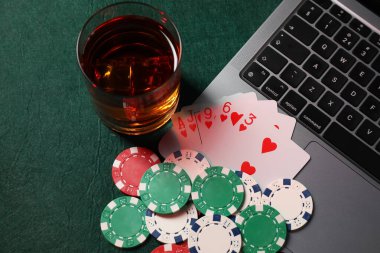 Poker fişleri, dizüstü bilgisayar, iskambil kağıtları ve yeşil masada bir bardak alkol. Çevrimiçi oyun