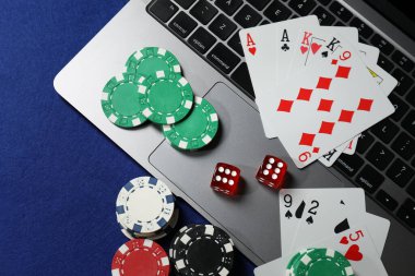 Poker fişleri, dizüstü bilgisayar, kağıt ve zarlar mavi masada, düz konum. Çevrimiçi oyun