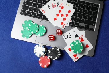 Poker fişleri, dizüstü bilgisayar, kağıt ve zarlar mavi masada, düz konum. Çevrimiçi oyun