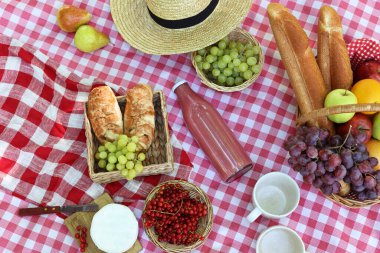 Lezzetli yemekler, masa örtüsü ve içeceklerle dolu piknik sepeti.