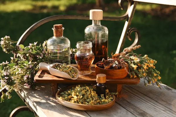 stock image Different tinctures in bottles, bark chips and flowers on wooden bench outdoors