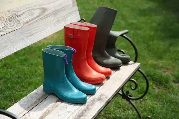 stock image Three pairs of rubber boots on wooden bench outdoors