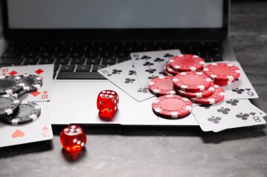 Poker fişleri, dizüstü bilgisayar, gri desenli masada kağıt ve zarlar. Çevrimiçi oyun
