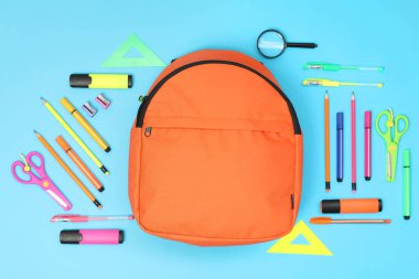 Sırt çantası ve açık mavi arka planda farklı okul malzemeleri.