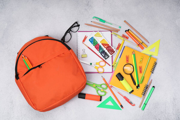 Flat lay composition with backpack and different school stationery on light grey table