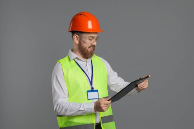 Kask ve gözlüklü mühendis gri arka planda pano tutuyor.
