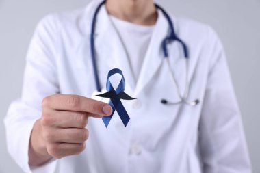 Prostat kanseri farkındalığı. Açık gri arka planda sahte bıyıklı mavi kurdele tutan doktor, yakın plan.