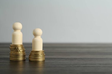 Finansal eşitsizlik. Ahşap masada insan figürleri ve madeni paralar. Metin için boşluk
