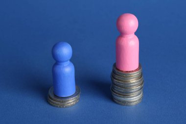 Finansal eşitsizlik. Erkek ve kadın figürleri mavi arkaplana karşı farklı yükseklikte istiflenmiş paralar üzerinde