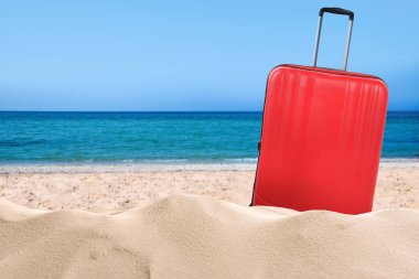 Denize yakın kumsalda kırmızı bir bavul. Metin için boşluk