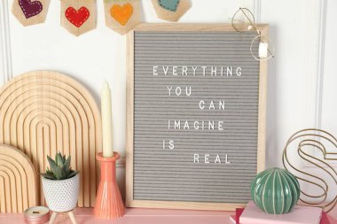 Letter board with phrase Everything You Can Imagine Is Real and decor elements on pink wooden table clipart