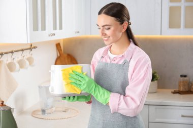 Güzel genç bir kadın mutfakta tost makinesini bez parçasıyla siliyor.