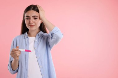 Pembe arka planda hamilelik testi tutan üzgün kadın, mesaj için boşluk