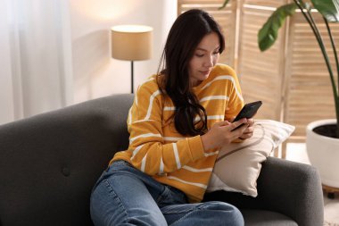 Evdeki kanepede akıllı telefonlu güzel bir kadın.