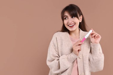 Açık kahverengi arkaplan üzerinde hamilelik testi olan mutlu genç kadın, mesaj için boşluk