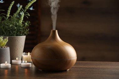 Aroma yağı yayıcı, yanan mumlar ve ahşap masa üzerinde bitkiler, metin için yer