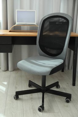 Gri sandalye, dizüstü bilgisayar ve masa ofiste.