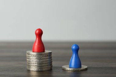 Finansal eşitsizlik. Ahşap masada insan figürleri ve madeni paralar