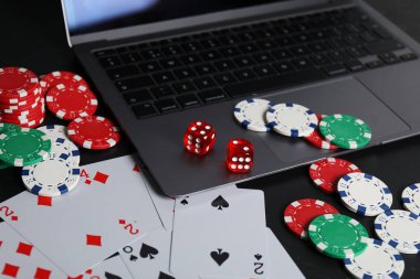 Çevrimiçi poker. Siyah masada kart, fiş, zar ve dizüstü bilgisayar oynanıyor.