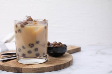 Tasty milk bubble tea in glass, tapioca pearls and straws on white marble table, space for text clipart