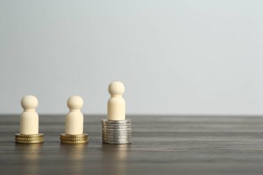 Finansal eşitsizlik. Ahşap masada insan figürleri ve madeni paralar. Metin için boşluk