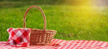 Güneşli bir günde yeşil çimlerin üzerinde piknik battaniyesi ve hasır sepet. Metin için alanı olan pankart tasarımı