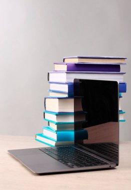 Açık gri arkaplana karşı beyaz ahşap masa üzerinde renkli kitap ve dizüstü bilgisayar yığını