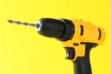 Sarı arka planda modern kablosuz elektrikli matkap, yakın plan.