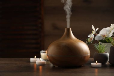 Aroma yağı yayıcı, yanan mumlar ve ahşap masa üzerinde bitkiler.