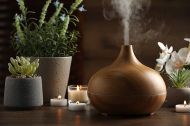 Aroma yağı yayıcı, yanan mumlar ve ahşap masa üzerinde bitkiler.