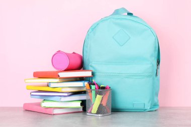 Açık gri masada pembe arka planda farklı okul kırtasiyesine sahip sırt çantası