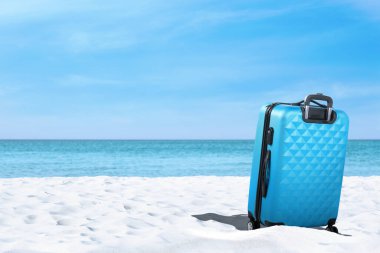 Denize yakın kumsalda açık mavi bir bavul. Metin için boşluk